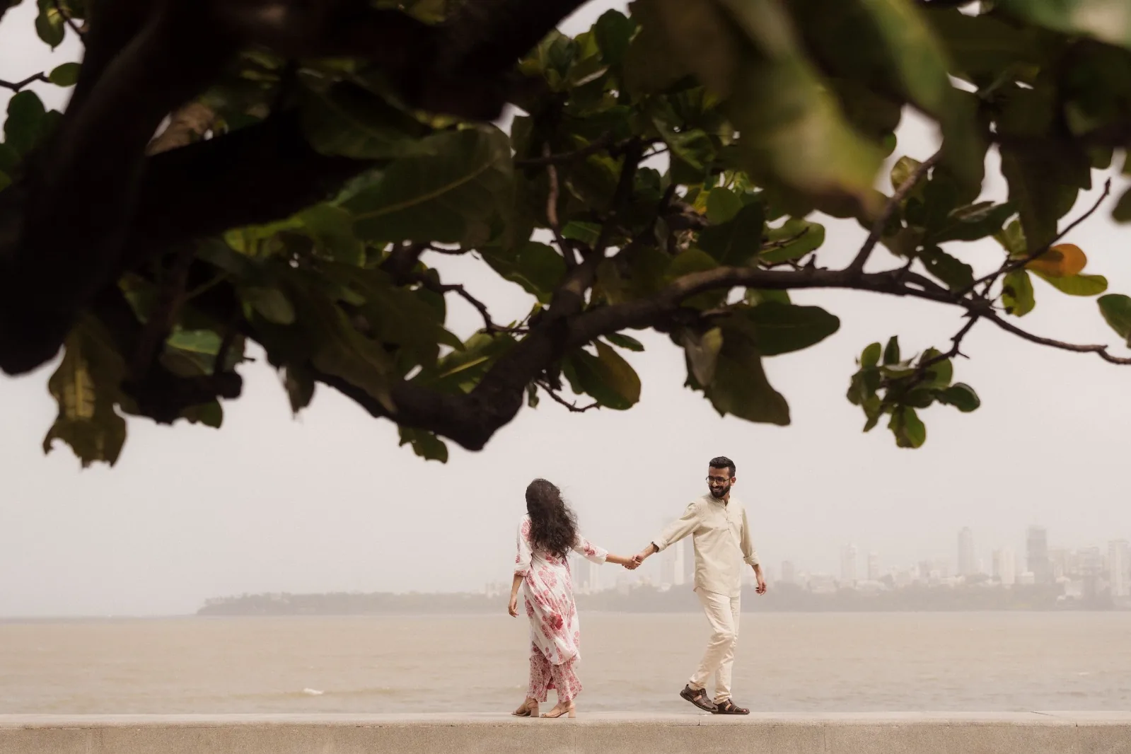 Holding hands on the sea wall beneath a great tree