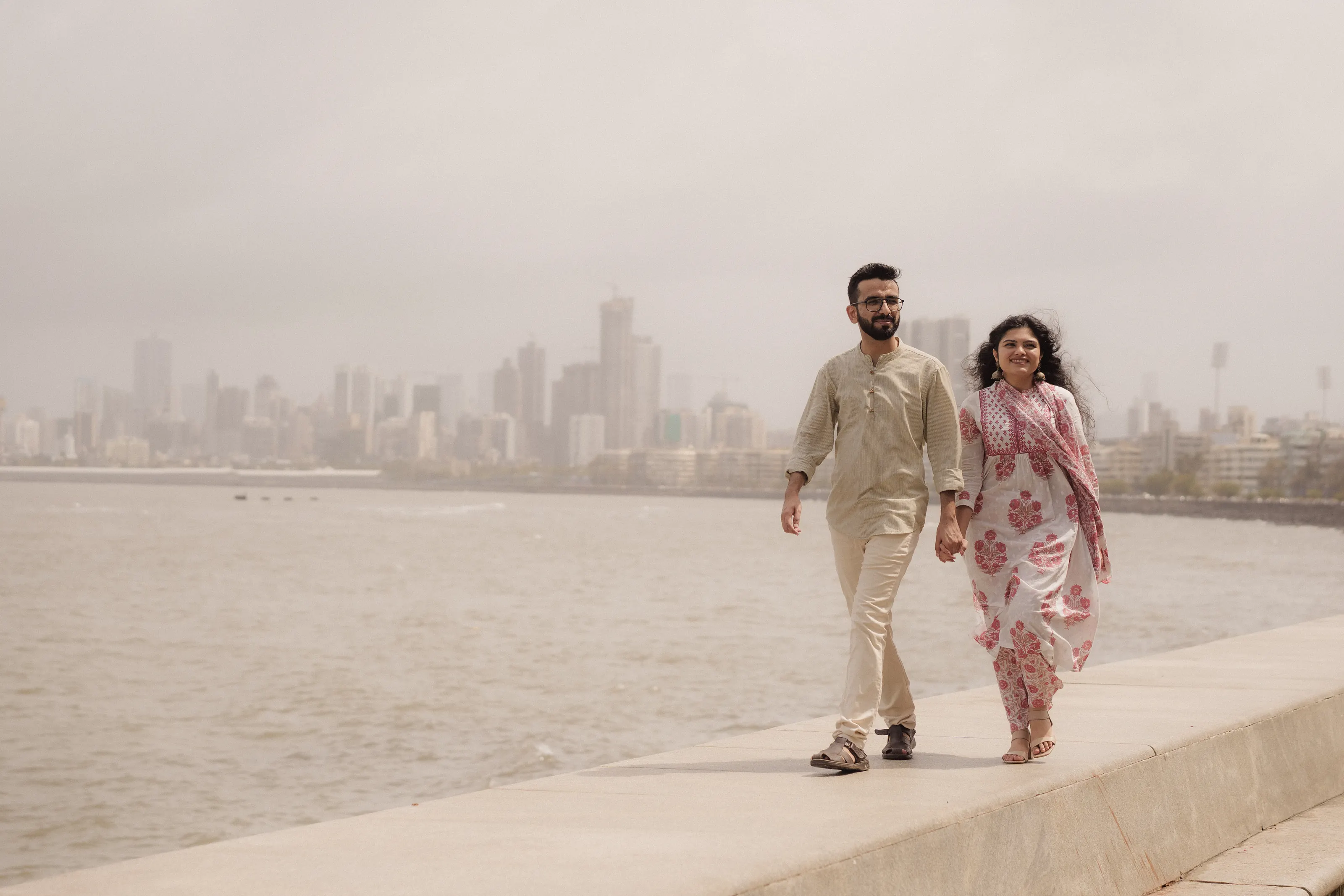 Walking hand in hand along the Marine Drive sea wall, the Mumbai skyline behind them